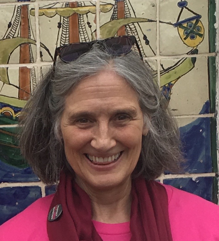 photo of Sabriga in a pink shirt smiling in front of a mosaic wall and with her sunglasses propped up on the top of her head